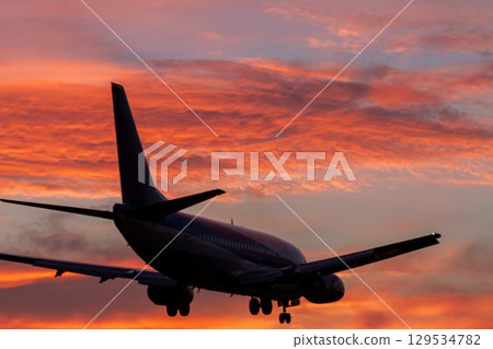 A burning sunset sky and a landing passenger plane A burning sunset sky and a landing passenger plane 129534782