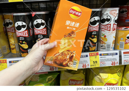 A woman's hand holding potato chips with chicken flavor inside a supermarket 129535102