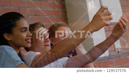 Image of financial graph over happy diverse pupils taking selfie at school 129537578