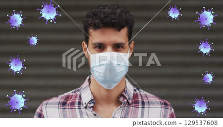Image of falling covid 19 cells over man wearing face mask 129537608