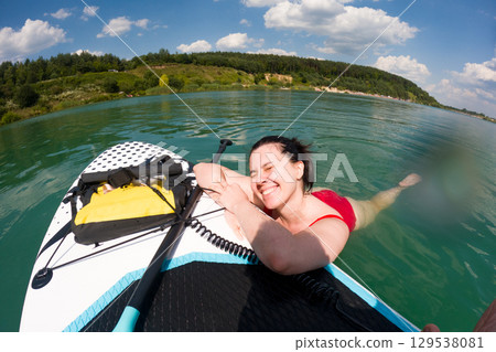Woman Smiling on Paddleboard in Serene Lake 129538081