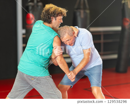 Elderly man learning self-defense grips and escapes at gym 129538296