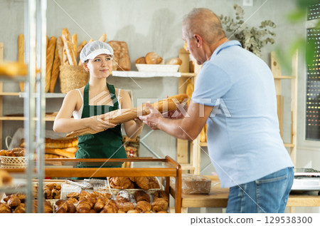 Young woman seller selling baguettes to man buyer Young woman seller selling baguettes to man buyer 129538300