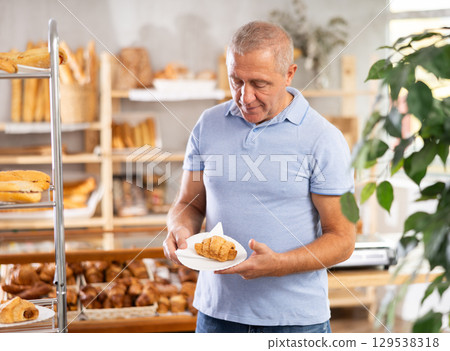 Elderly man with fresh croissant in bakery 129538318