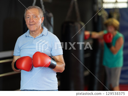 Elderly man trains in the gym - practicing punches on punching bag Elderly man trains in the gym - practicing punches on punching bag 129538375