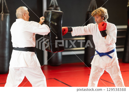 Karate student punching shield under guidance of experienced partner Karate student punching shield under guidance of experienced partner 129538388