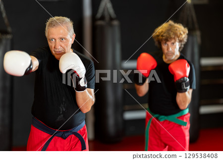 Elderly man trains in the gym - practicing punches on punching bag 129538408