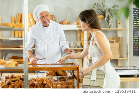 Girl selects and buys hot croissants at a bakery. Male salesperson places croissants in plastic bag 129538411