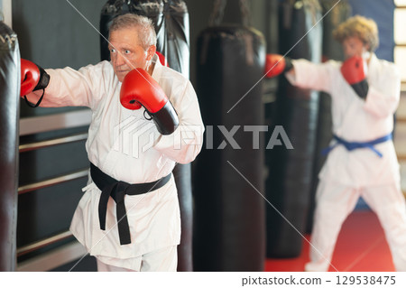 Elderly man in white kimono practices punching punching bag 129538475