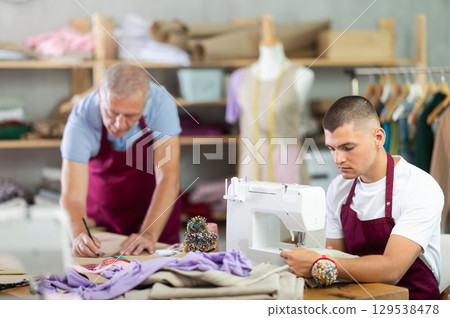 Young guy sews on machine male assistant drawing pattern 129538478