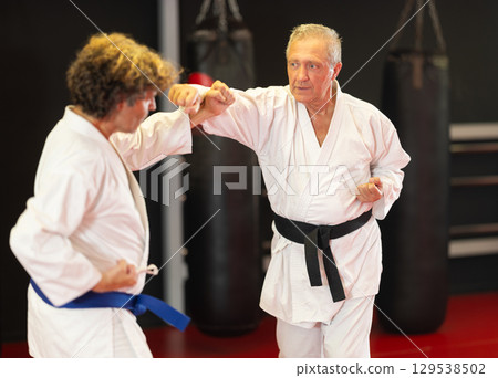Older karate fighter practicing paired kumite in dojo Older karate fighter practicing paired kumite in dojo 129538502