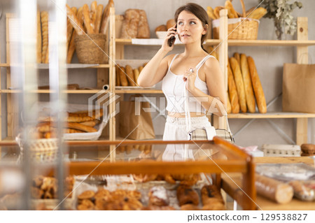 European girl in bakery is talking on phone, inspecting goods in window European girl in bakery is talking on phone, inspecting goods in window 129538827