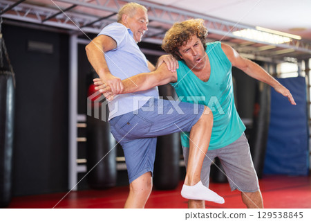 Mature man and adult man practice self-defense techniques at gym Mature man and adult man practice self-defense techniques at gym 129538845