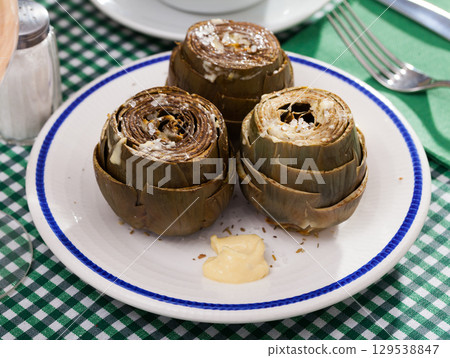 Delicious steamed artichoke with alioli sauce on a white plate Delicious steamed artichoke with alioli sauce on a white plate 129538847