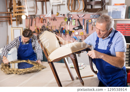 To replace upholstery, restorer removes old cloth seat covering from antique wooden chair. 129538914
