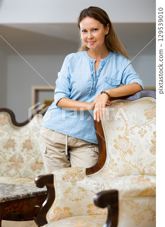 Positive woman standing near sofa at home 129539010