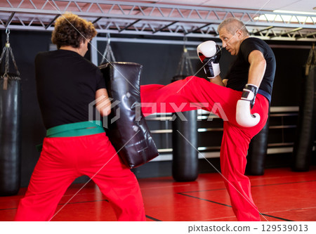 Man punches boxing paw held by trainer 129539013