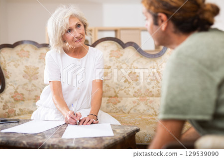Helpful man helping elderly woman to sign documents 129539090