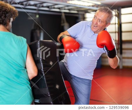 Elderly man striking shield in self‑defense drill Elderly man striking shield in self‑defense drill 129539096
