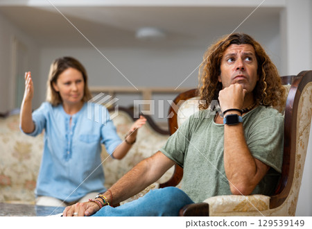 Middle-aged male and female settling relations between themselves sitting on the couch Middle-aged male and female settling relations between themselves sitting on the couch 129539149