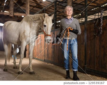 Mature woman with a white horse in stable 129539167