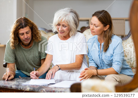 Positive couple and old woman taking notes on the sofa at home 129539177