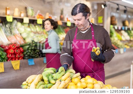 Adult man seller puts bananas on display Adult man seller puts bananas on display 129539193