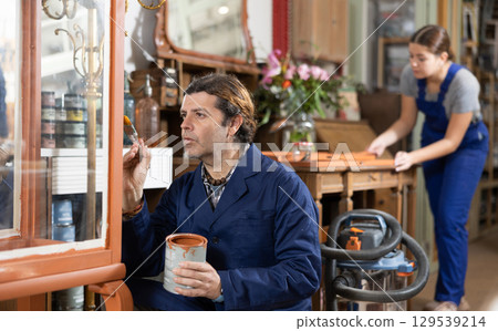Male furniture maker diligently working on vintage glass cabinet in workshop Male furniture maker diligently working on vintage glass cabinet in workshop 129539214