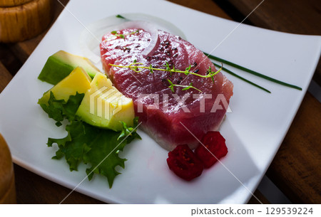 Delicious pieces raw tuna, green avocado and greens at plate Delicious pieces raw tuna, green avocado and greens at plate 129539224