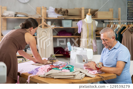 Senior man employee sewing, stitch clothes, girl apprentice draw dress pattern 129539279