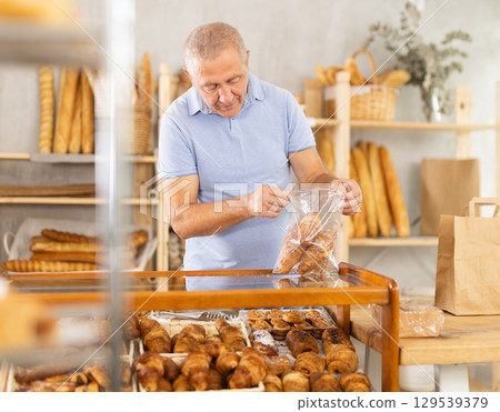 European senior man visitor puts croissant in plastic disposable bag 129539379