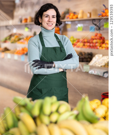Woman store employee in apron and gloves stands in sales area of vegetable 129539393