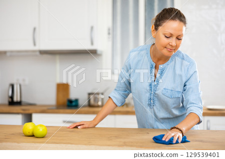 Positive female using a rag for cleaning tabletop at cozy apartment 129539401