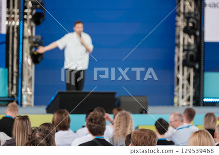 Speaker engaging with audience during a presentation on blue stage 129539468