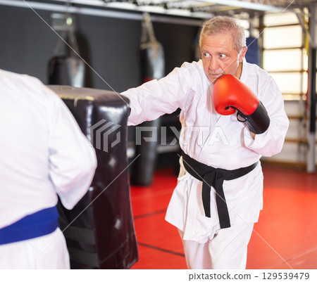 Older karate practitioner punching shield in training dojo Older karate practitioner punching shield in training dojo 129539479