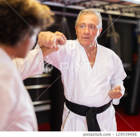 Older karate fighter practicing paired kumite in dojo 129539498