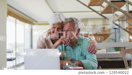 Image of falling icons over caucasian senior couple using laptop Image of falling icons over caucasian senior couple using laptop 129540022
