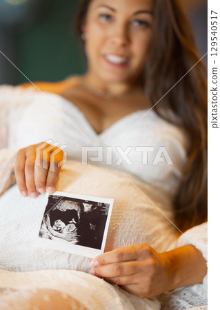 Pregnant Woman Holding Ultrasound Image of Baby in Womb in White Dress Pregnant Woman Holding Ultrasound Image of Baby in Womb in White Dress 129540517