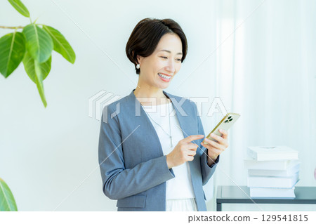 經營一部智能手機的女商人在辦公室 經營一部智能手機的女商人在辦公室 129541815