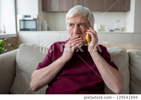 Suspicious elderly man with phone at home, targeted by scam artists, telemarketing fake news Suspicious elderly man with phone at home, targeted by scam artists, telemarketing fake news 129541894
