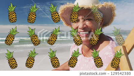 Image of pineapple over happy senior woman sunbathing on beach 129542380