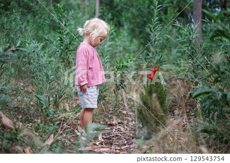 Little European girl standing by a small fir tree in the forest, looking sad Little European girl standing by a small fir tree in the forest, looking sad 129543754
