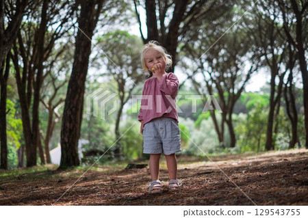 Blonde European girl in shorts standing in the forest eating a pear Blonde European girl in shorts standing in the forest eating a pear 129543755