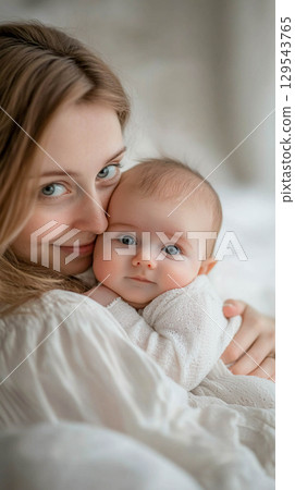 A woman holds a baby in her arms. The woman gently cuddles the baby. 129543765