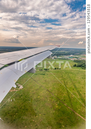 View of airplane wing, blue skies and green land during landing. Airplane window view. View of airplane wing, blue skies and green land during landing. Airplane window view. 129543818
