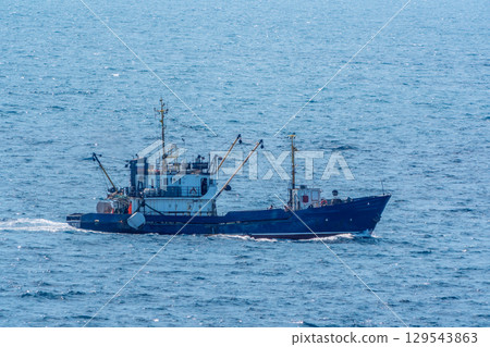 Fishing boat in blue sea and clear sky with birds flying overhead. Fishing boat in blue sea and clear sky with birds flying overhead. 129543863