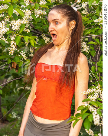 Young woman sneezes in the park against the background of a flowering tree. Allergy to pollen concept. 129543870