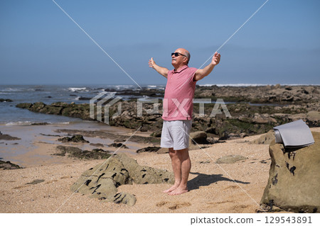 An elderly Spanish man exercising on the beach, stretching his arms. An elderly Spanish man exercising on the beach, stretching his arms. 129543891