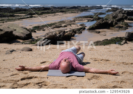 An elderly Spanish man exercising on the beach, stretching his arms. 129543926
