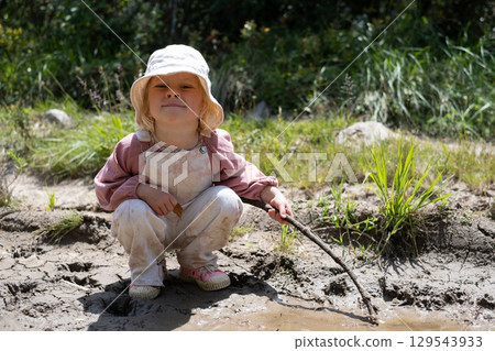 A 3-year-old blonde girl playing in a muddy puddle. A 3-year-old blonde girl playing in a muddy puddle. 129543933